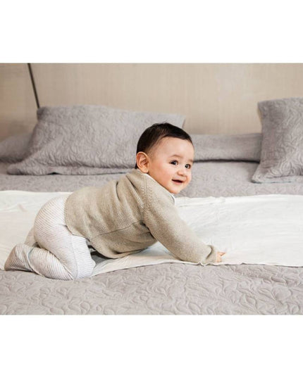 Bebé sonriente sobre una cama con un pañuelo de lactancia de algodón crudo de Amamantas.