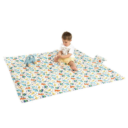 Manta impermeable infantil con diseño de dinosaurios coloridos sobre fondo blanco, ideal para picnic y playa. Niño sentado sobre la manta disfrutando al aire libre. Producto de Amamantas.