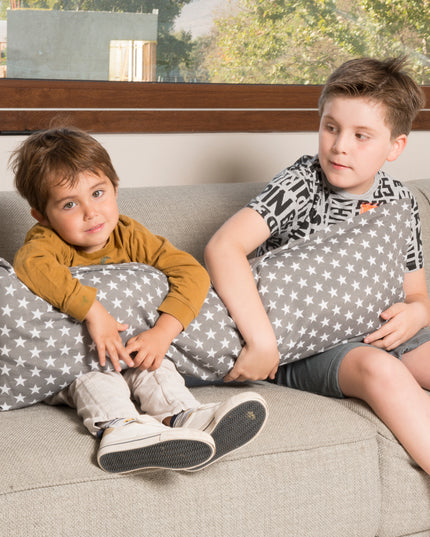 Dos niños sentados en un sofá abrazan un cojín XL de 90cm en color grafito con diseño de estrellas de Amamantas.