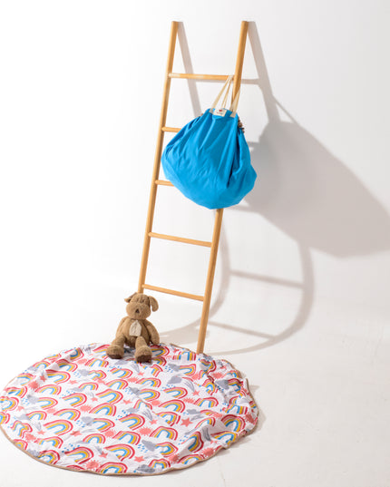 Manta 2 en 1 para niños con diseño de arcoíris colorido sobre fondo blanco, hecha de algodón orgánico, ideal como alfombra o bolsa. Amamantas.