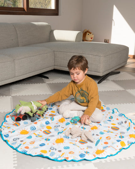 Niño jugando sobre una manta 2 en 1 con diseño espacial, colores vibrantes y borde azul. Ideal como alfombra y bolsa de juguetes. Amamantas.
