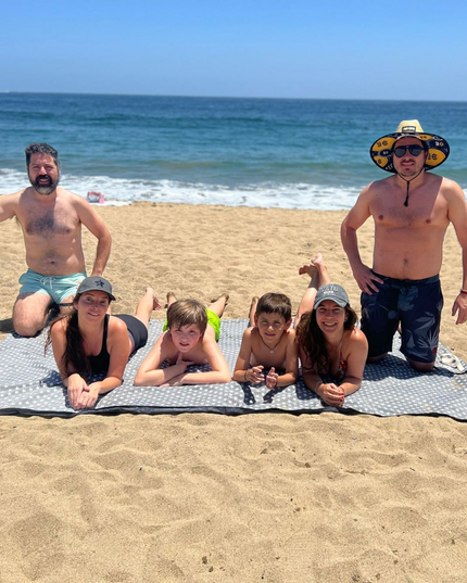 Familia disfrutando en la playa sobre la Manta JUMBO GIGANTE de Amamantas, ideal para picnic y playa, en color grafito.